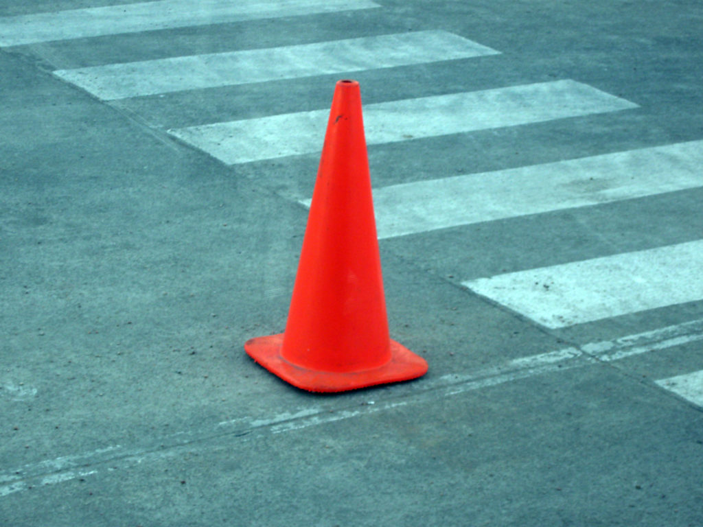 An orange safety cone on a road beside a crosswalk