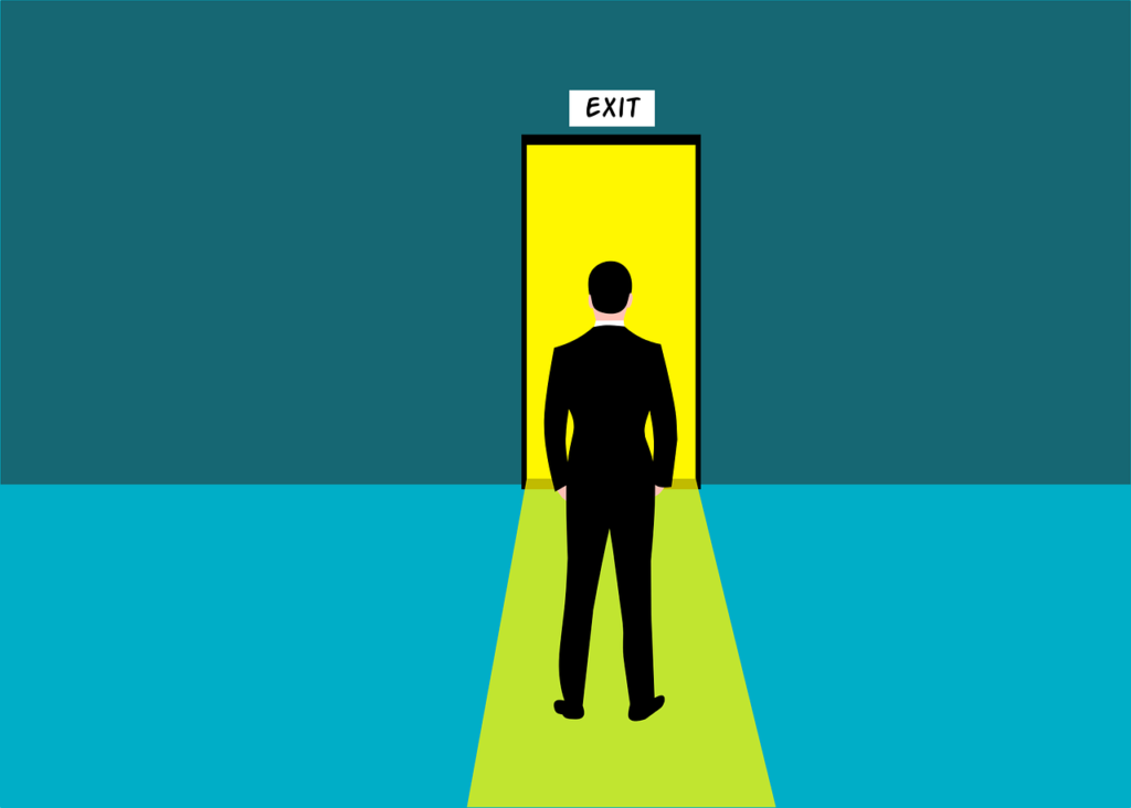A man in a business suit in front a door with an exit sign. 